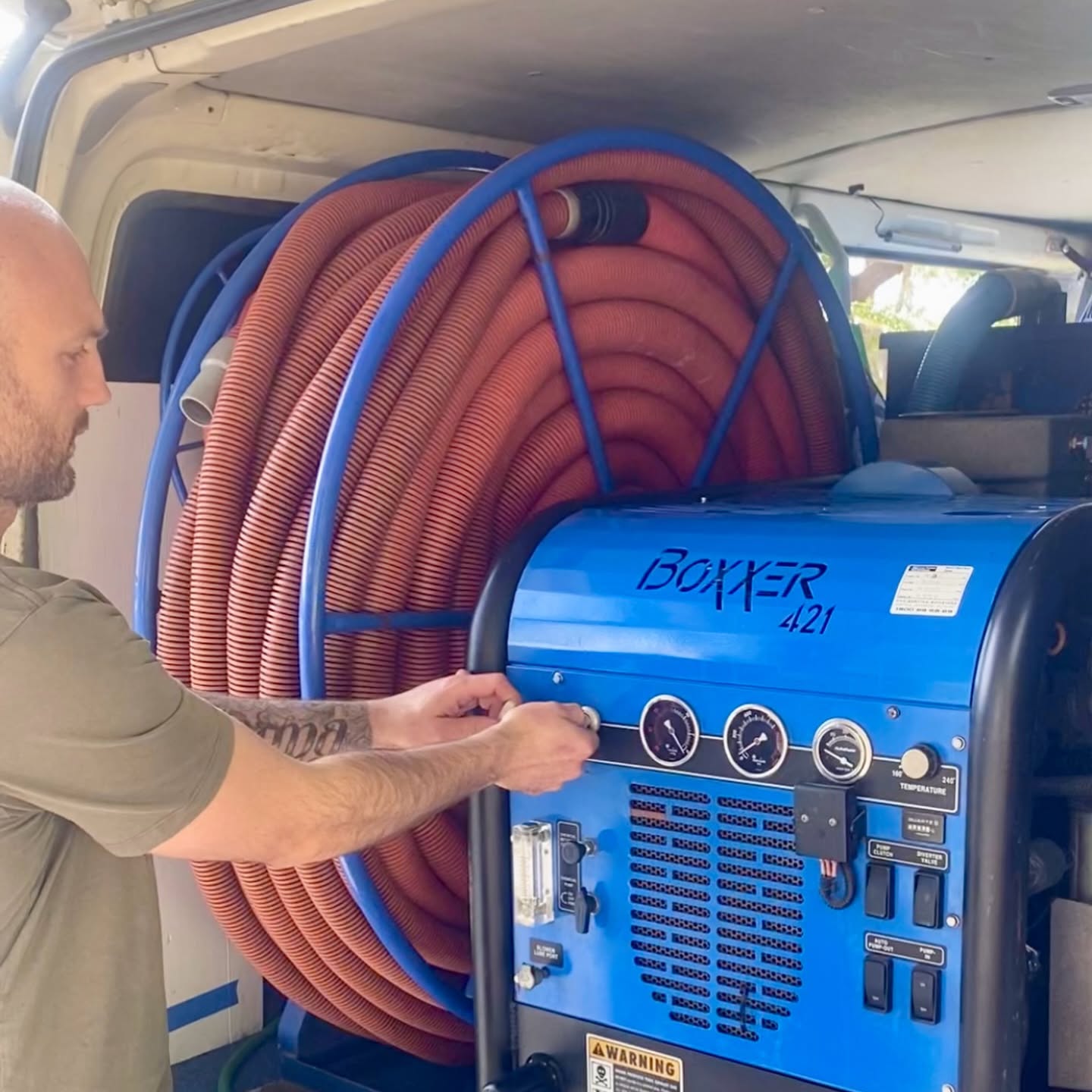 Technician at the truck-mounted carpet cleaning machine and hose reels inside the Natural Breeze van
